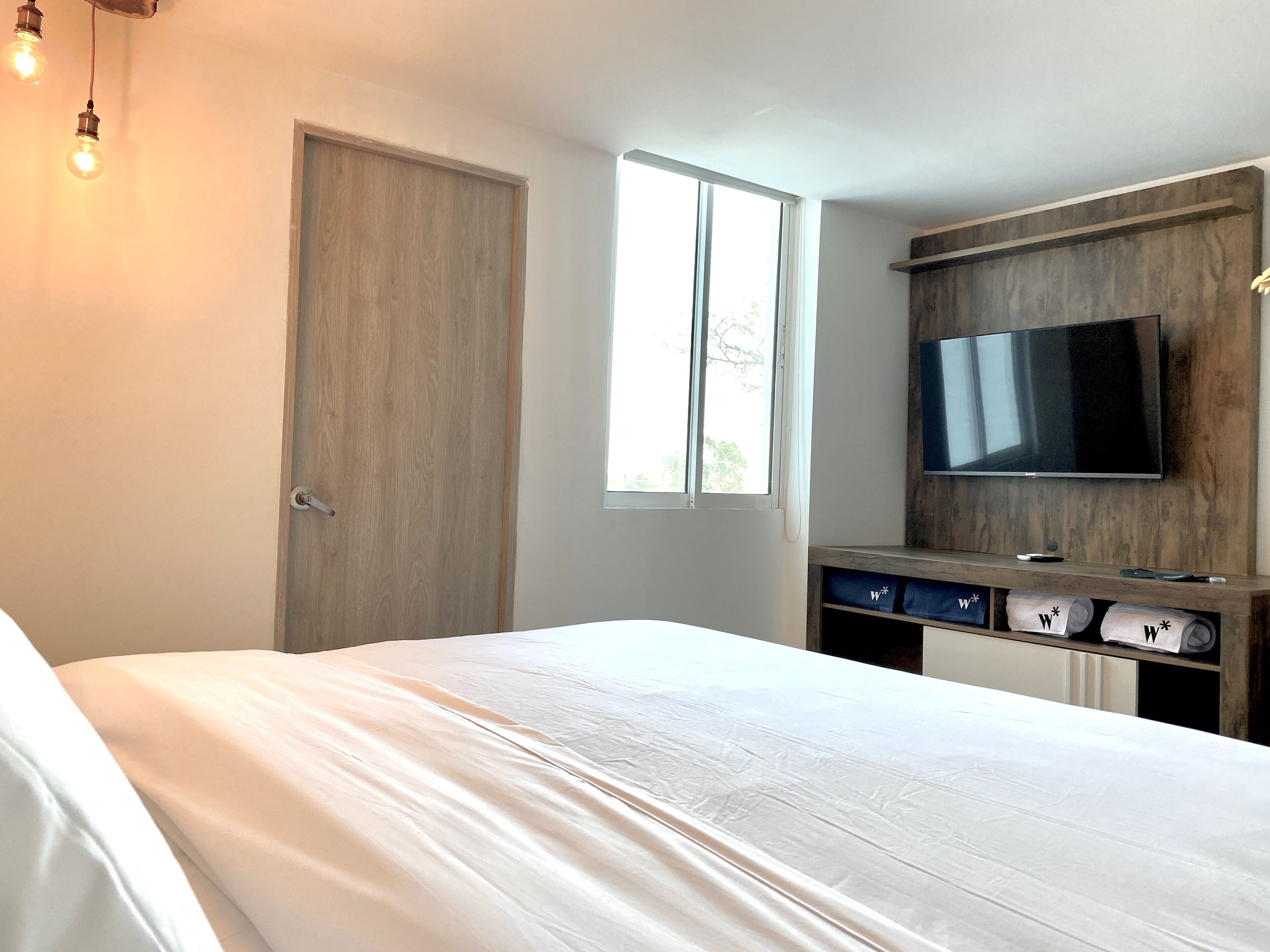 Ein Schlafzimmer mit einem Bett, einem Holzschrank, einem an der Wand montierten Fernseher und einem Fenster für natürliches Licht.