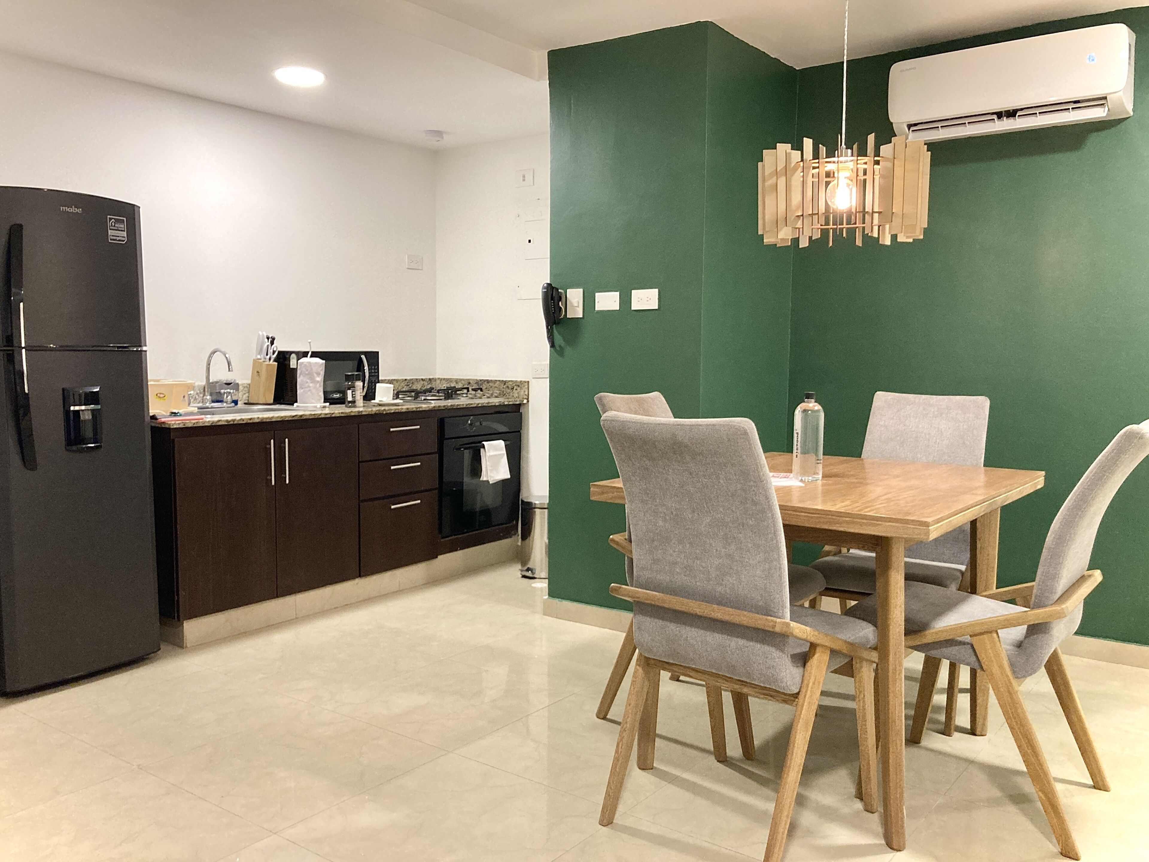 A modern kitchen with dark cabinets, a black refrigerator, and a wooden dining table with four grey chairs.
