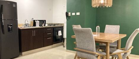 A modern kitchen with dark cabinets, a black refrigerator, and a wooden dining table with four grey chairs.