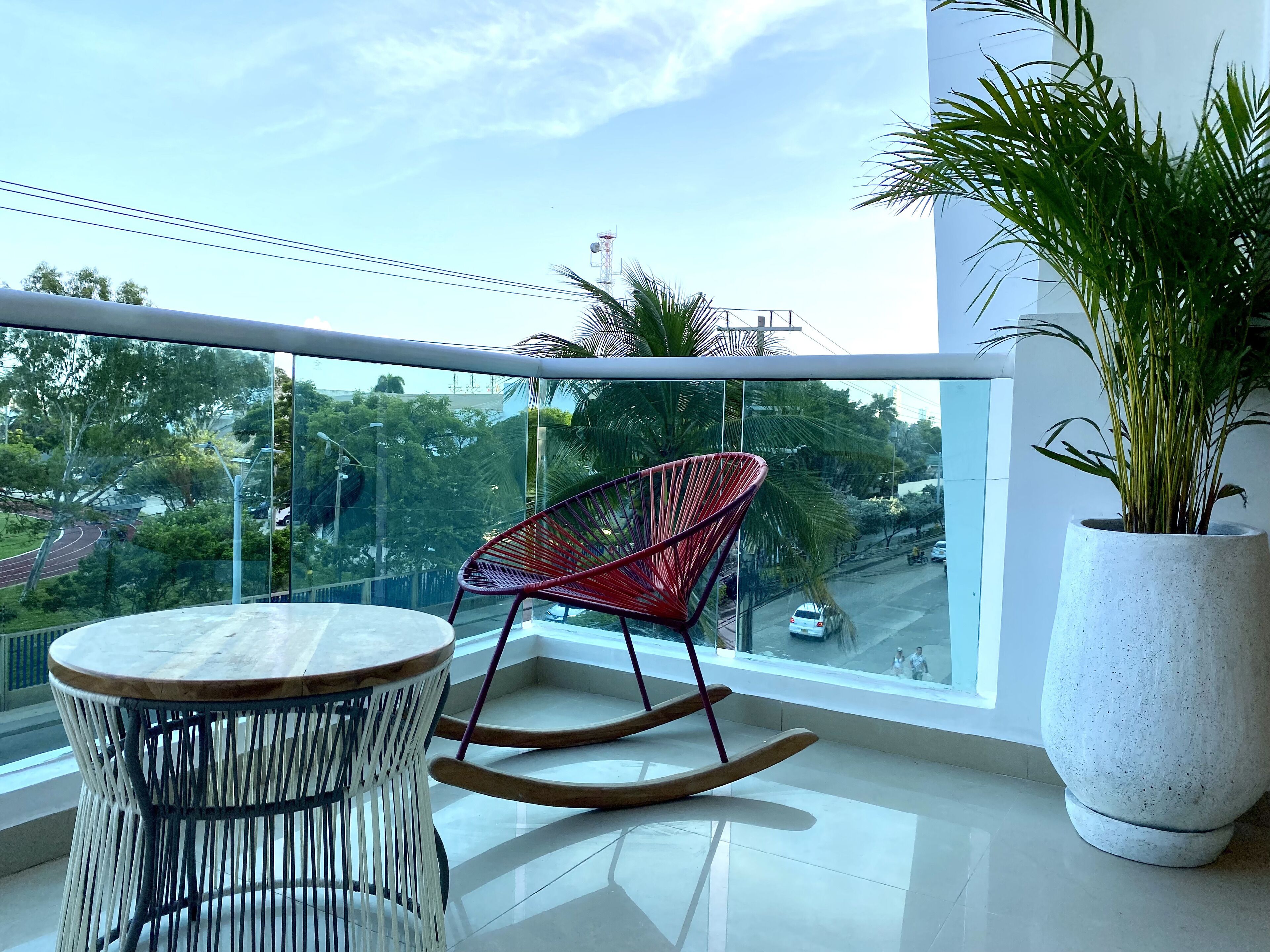 A balcony with a round table, a red rocking chair, and a large potted plant.
