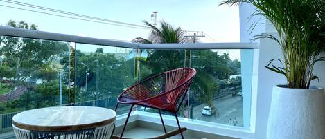 A balcony with a round table, a red rocking chair, and a large potted plant.