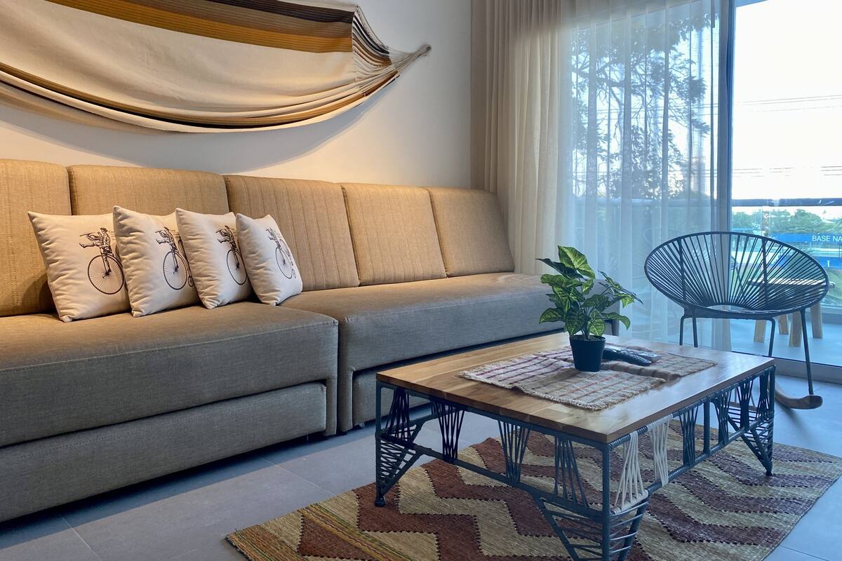Un salon moderne avec un canapé, une table basse, un fauteuil et une grande fenêtre avec des rideaux.