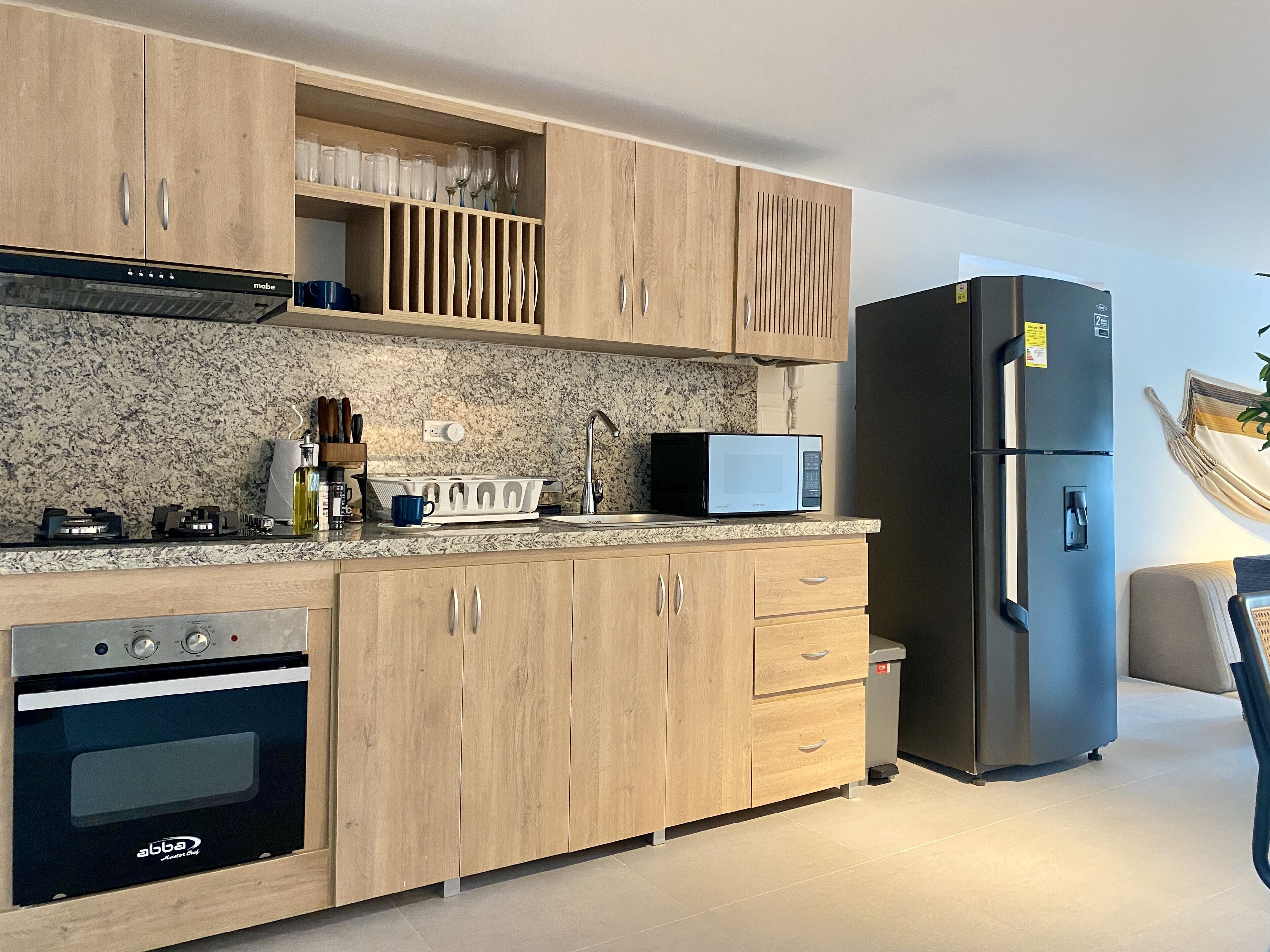 Una cocina moderna con armarios de madera, microondas integrado, refrigerador de acero inoxidable y horno.