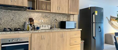 Una cocina moderna con armarios de madera, microondas integrado, refrigerador de acero inoxidable y horno.