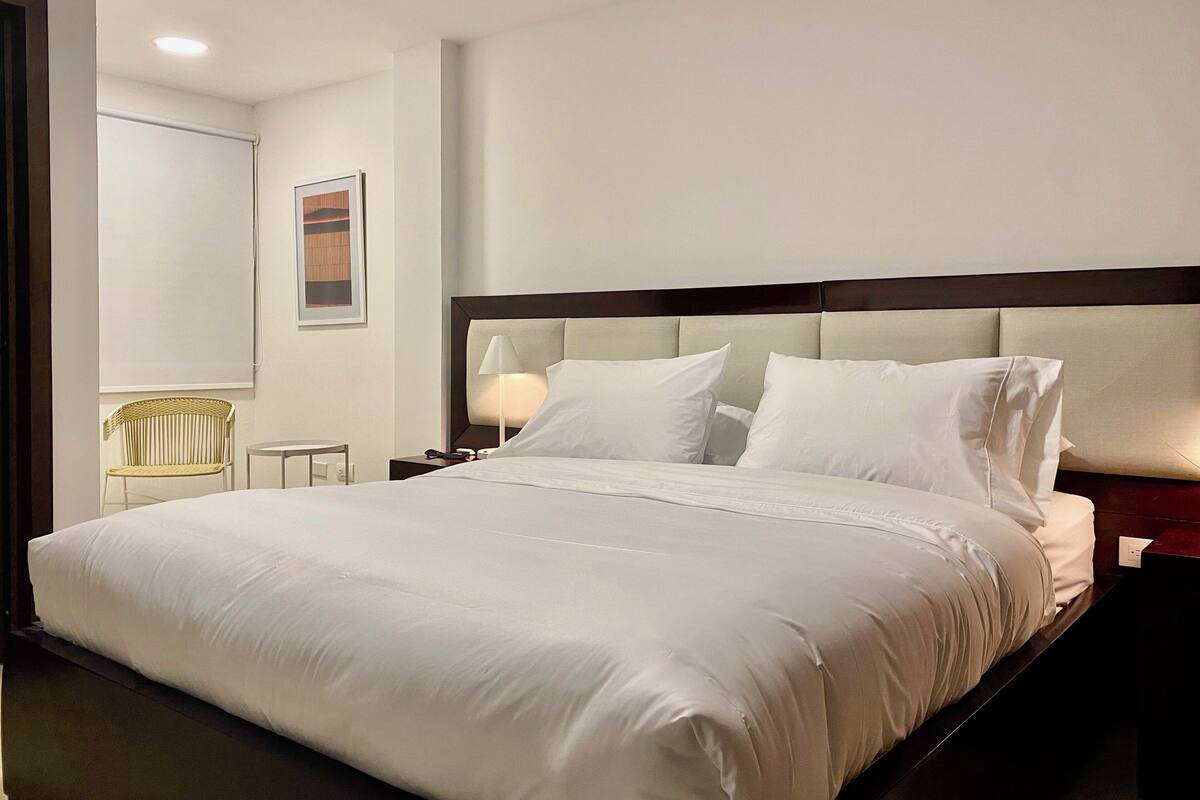 Une chambre d’hôtel avec un grand lit, une table de chevet avec une lampe, une chaise et un tableau encadré au mur.