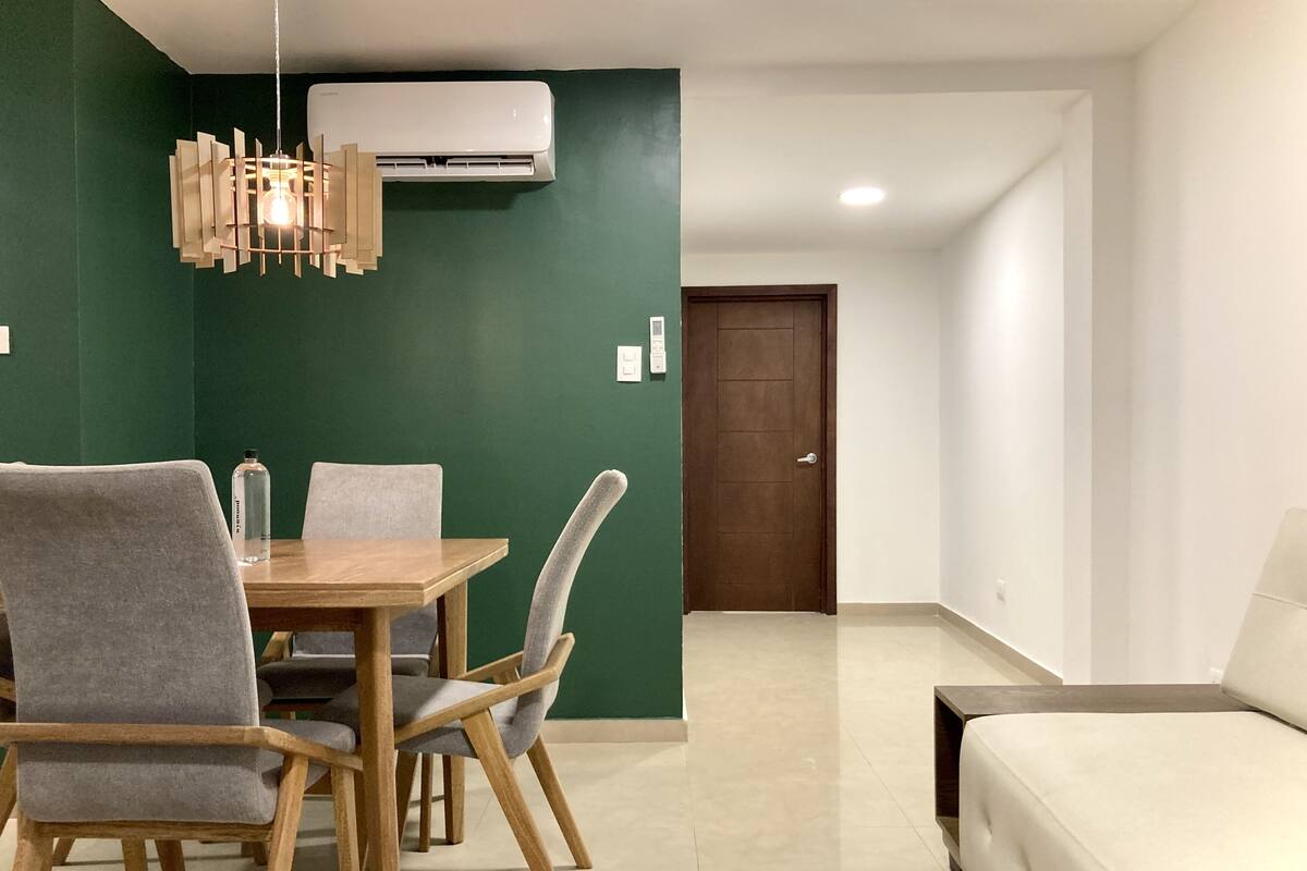 Un coin repas avec une table et des chaises en bois, un luminaire suspendu et un mur d’accent de couleur verte.