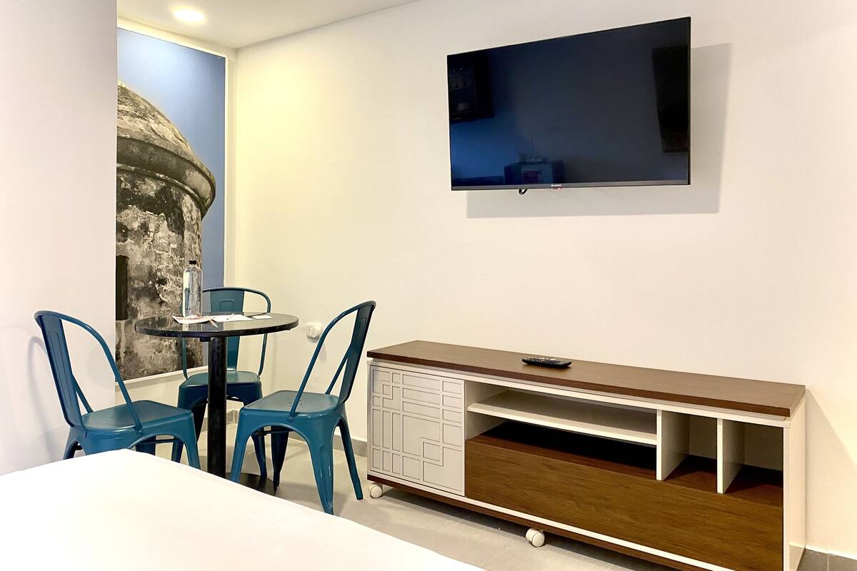 Une chambre avec un lit, un bureau avec une télévision et deux chaises.
