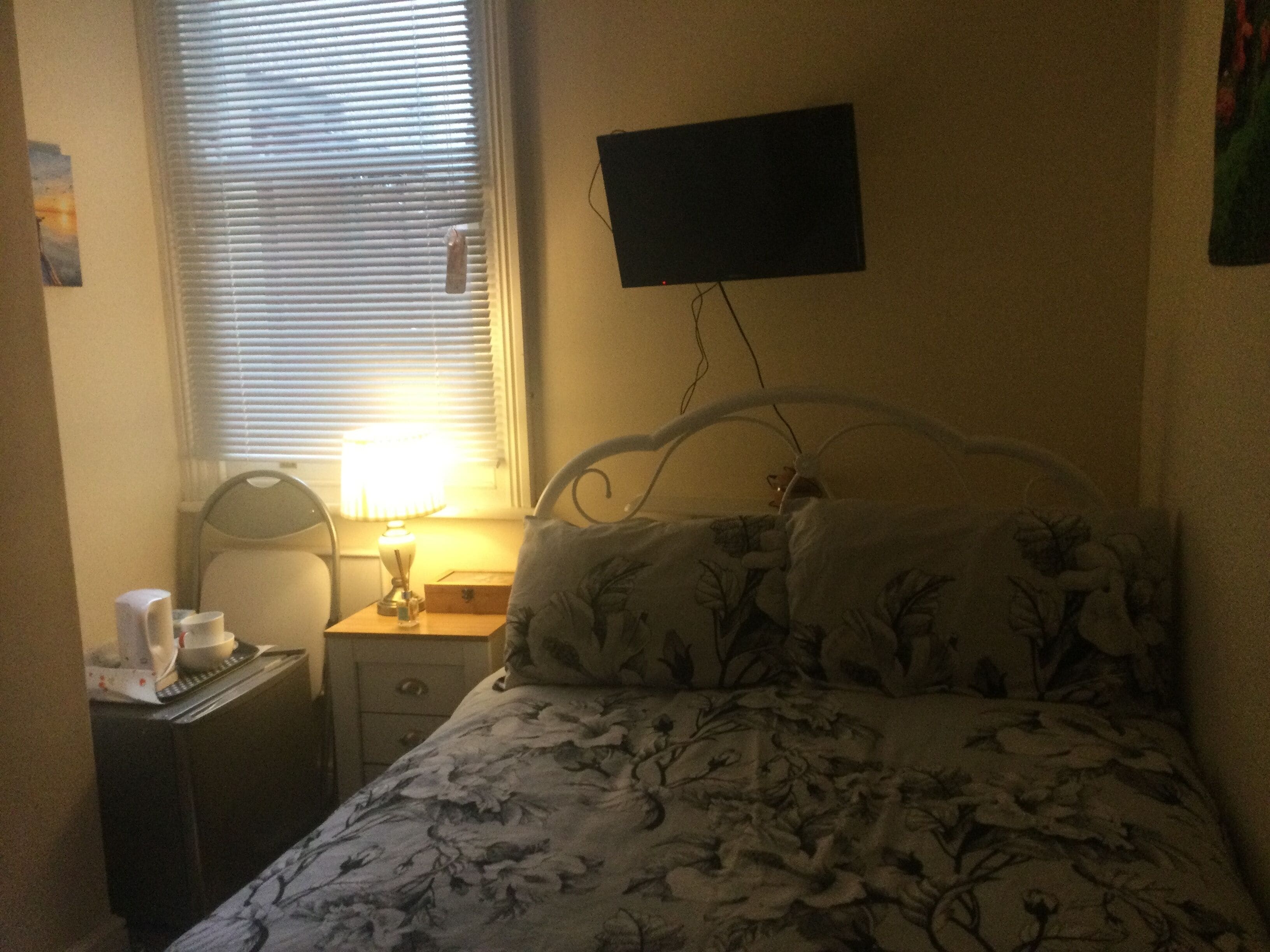 Un dormitorio con cama, una mesita de noche con lámpara, una mesita auxiliar y un televisor montado en la pared.