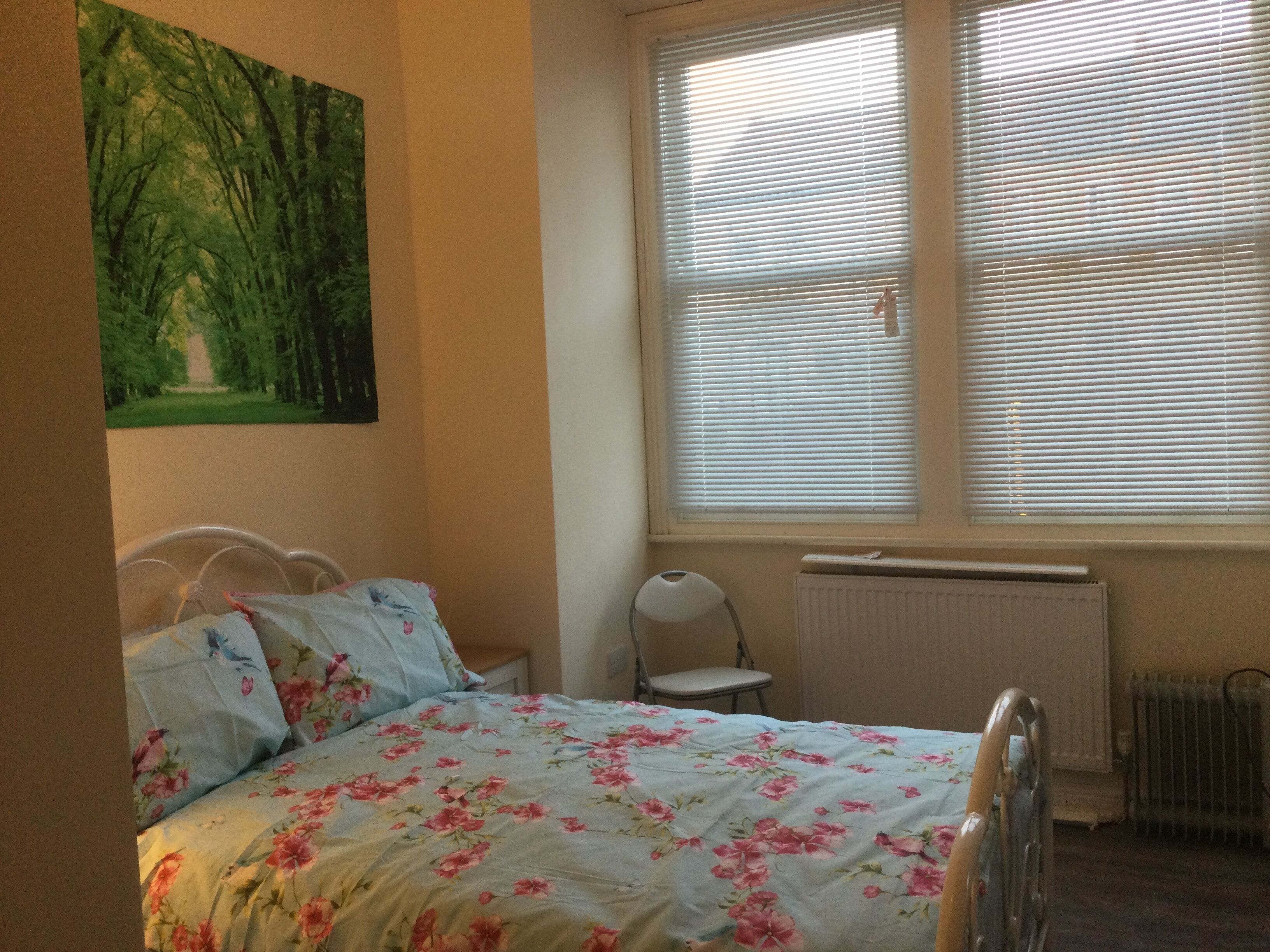 Une chambre à coucher avec un lit, une chaise, un radiateur et une fenêtre avec des stores.