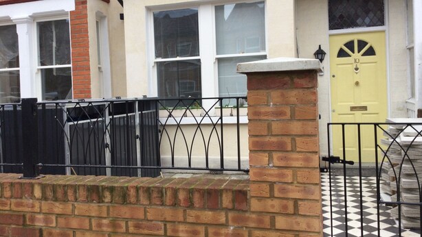 A residential building with a yellow door, brick walls, and a black metal fence. - TDM Bachelot Lettings Ltd (London)
