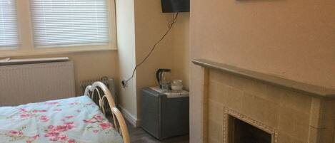 A bedroom with a bed, a fireplace, a radiator, a television mounted on the wall, and a window with blinds.