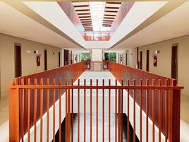 A modern hotel corridor with a central staircase, wooden railings, and a glass ceiling.