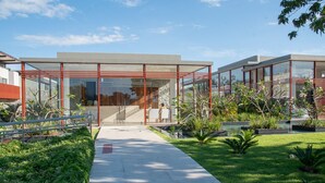 A modern building with large glass windows, a concrete pathway, and well-maintained greenery. - Flat Ilê de Pipa Sky - By Almare (Tibau do Sul)