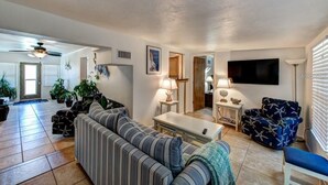 A spacious living room with a striped sofa, a coffee table, and a TV mounted on the wall. There are potted plants and a ceiling fan. - "Barracuda" (Bradenton)