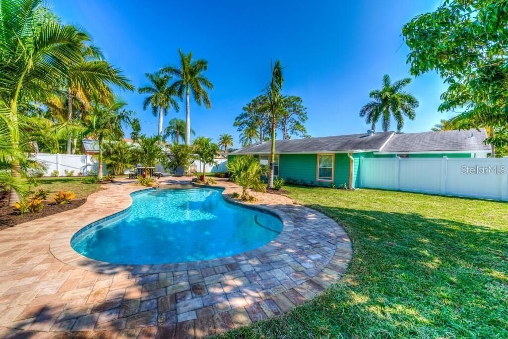 Una piscina con borde curvo, rodeada por un patio de ladrillo y palmeras.
