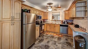 A kitchen with wooden cabinets, stainless steel appliances, a ceiling fan, and patterned floor tiles. - "Barracuda" (Bradenton)