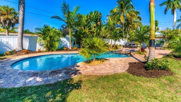 A backyard with a swimming pool, palm trees, and a patio area. - "Barracuda" (Bradenton)