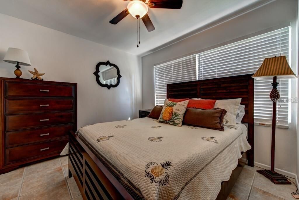 Un dormitorio con cama, cómoda, ventilador de techo, ventana con persianas y mesita de noche.