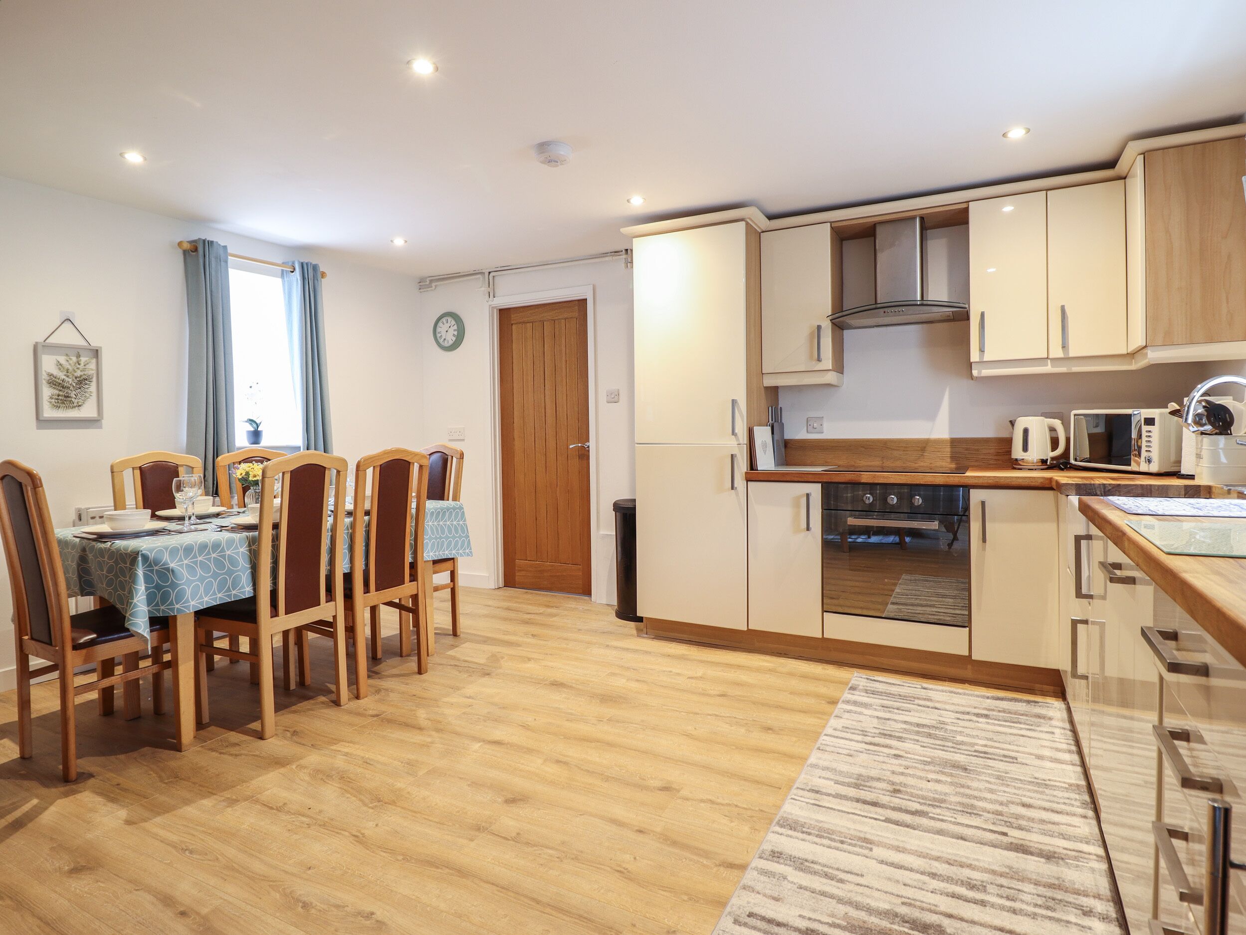 A modern kitchen with wooden cabinets, a built-in oven, and a dining area with a table and chairs.
