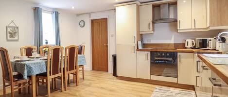 A modern kitchen with wooden cabinets, a built-in oven, and a dining area with a table and chairs.
