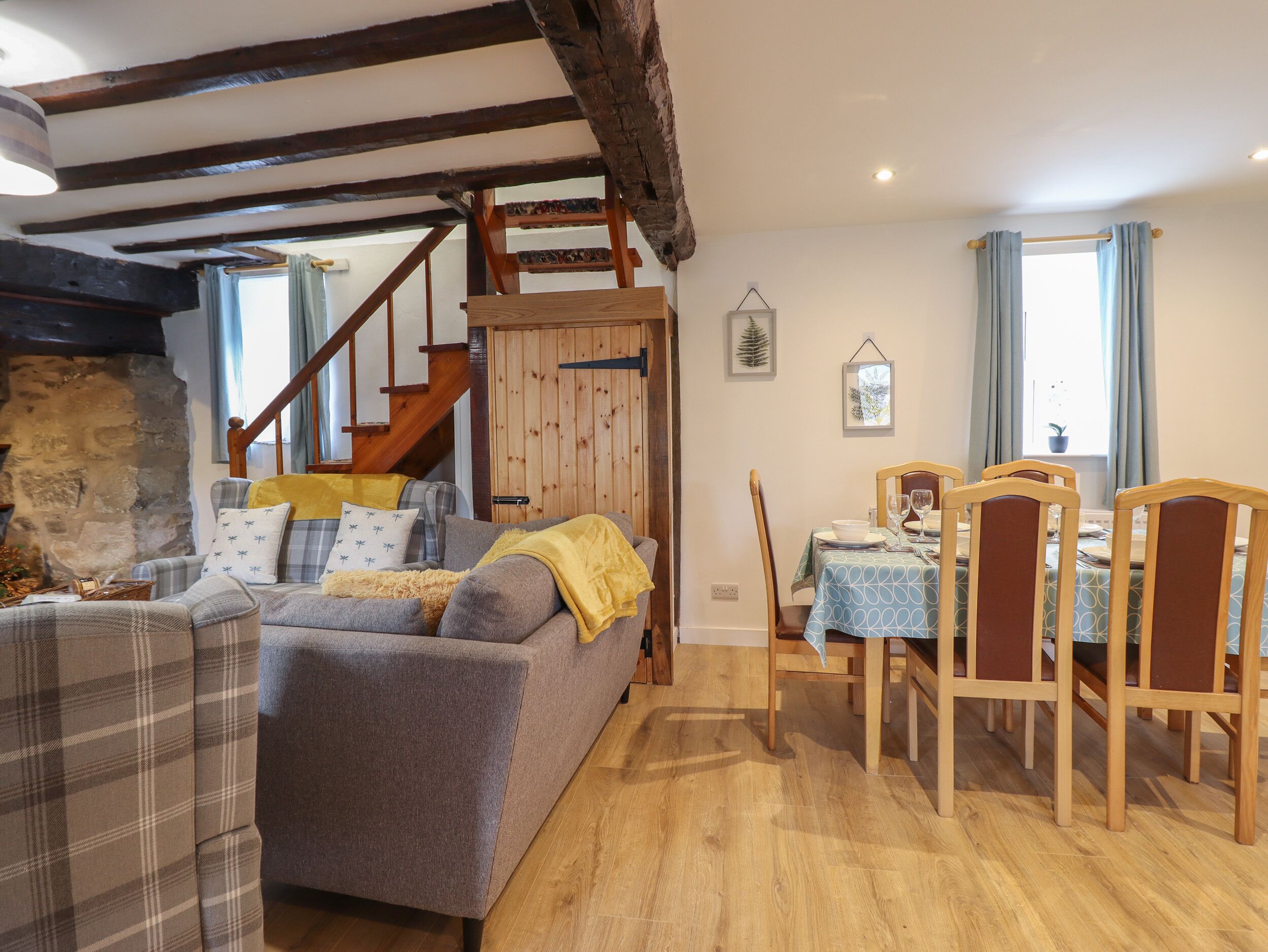 A cozy living room with a sofa, a dining table with chairs, a staircase, and a stone wall.