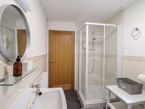 A bathroom with a glass-enclosed shower, a sink, a mirror, and a storage basket.