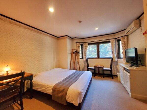 Ein Hotelzimmer mit Bett, Schreibtisch, Stuhl, Fernseher und einem fensterbepflanzten Fenster.