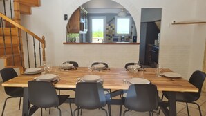 A dining area with a wooden table set for six, black chairs, and a view of the kitchen through an arched doorway. - Villa located in St Augustin, near Royan, 5km from the Grande Côte beach. (Saint-Augustin)
