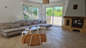 A modern living room with a sectional sofa, a small table, a wicker chair, and a stone fireplace. - Villa located in St Augustin, near Royan, 5km from the Grande Côte beach. (Saint-Augustin)