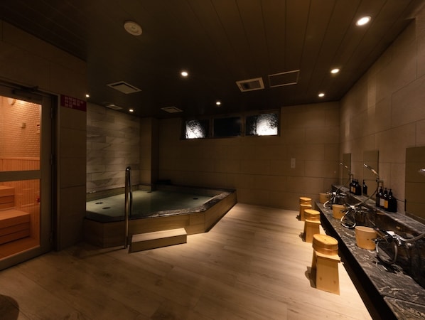 A sauna room with a wooden bench, a hot tub, and a counter with bottles and cups.