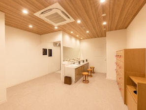 Un baño moderno con techo de madera, un espejo grande, tocador con varios lavamanos y un mueble de almacenamiento con cajones.