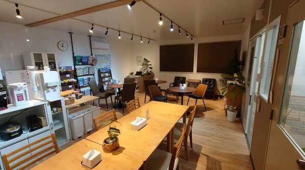 Ein modernes Café mit Holztischen und -stühlen, einer Kaffeemaschine sowie einer Auswahl an Snacks und Getränken auf Regalen.