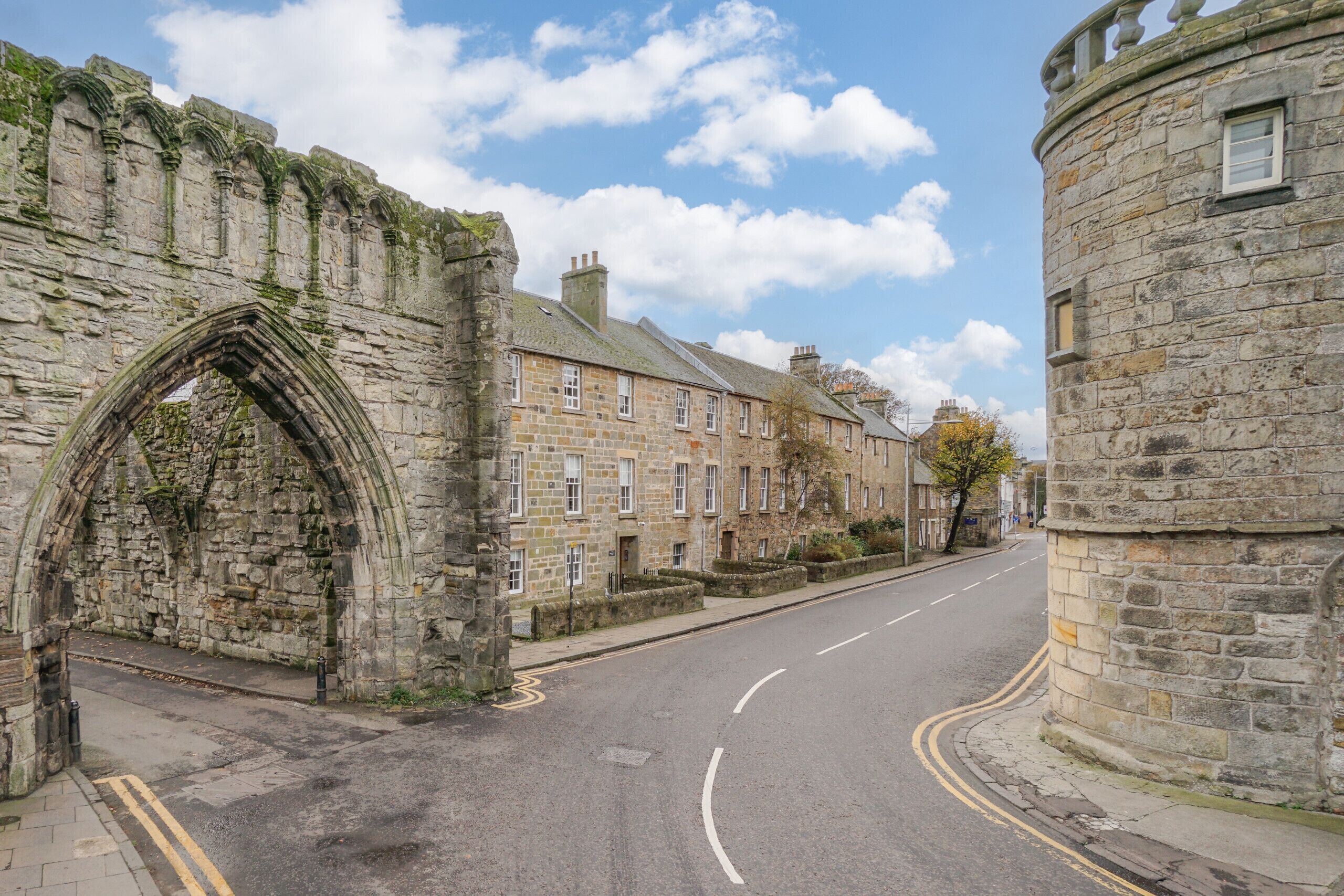 A street with stone buildings, including a large archway and a round tower.