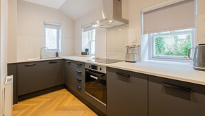 A modern kitchen with grey cabinets, a built-in oven, a window with a view, and a kettle on the counter.