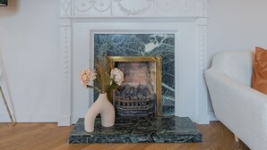 A fireplace with a marble surround, a vase with flowers, and a couch with a cushion. - Priorsgate | Oliphant Apartment (St Andrews)