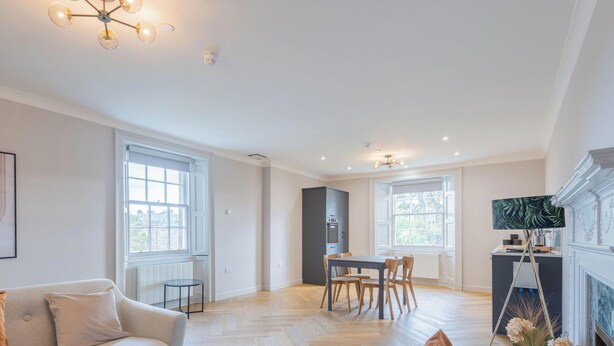 A spacious living room with a dining area, large windows, and a fireplace. - Priorsgate | Oliphant Apartment (St Andrews)