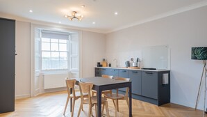 A modern kitchen with a dining table and chairs, a window with a view, and a whiteboard on the wall. - Priorsgate | Oliphant Apartment (St Andrews)