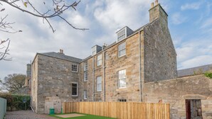 A stone building with multiple windows and a wooden fence. - Priorsgate | Oliphant Apartment (St Andrews)