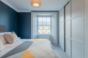 A bedroom with a bed, a window, and a view of buildings outside. - Priorsgate | Oliphant Apartment (St Andrews)