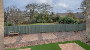 A courtyard with a wooden bench, a green fence, and a paved area with a brick pattern.