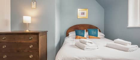 A bedroom with a bed, a dresser, a wall-mounted lamp, and a framed picture.