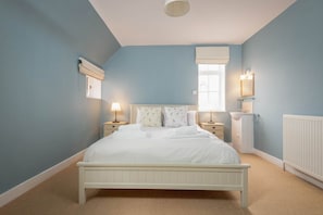 A bedroom with a bed, bedside tables, a window with a blind, a radiator, and a wall-mounted light fixture. - Stables Loft | Elie (Elie)