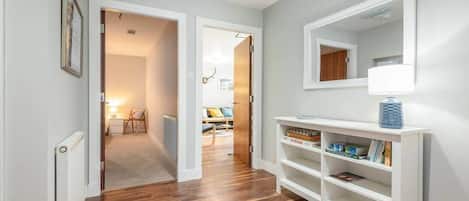 A hallway with wooden flooring, white walls, and a white console table with a lamp and books.