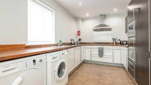 Une cuisine moderne équipée d’un lave-linge Bosch, d’un four encastré et d’un réfrigérateur en acier inoxydable.