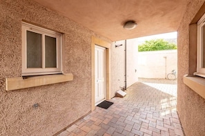 A narrow corridor with a window, a door, and a small step leading to a paved area.