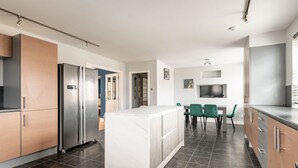 A modern kitchen with a central island, stainless steel appliances, and a dining area with green chairs. - Rosemount | Kilrenny (Kilrenny)