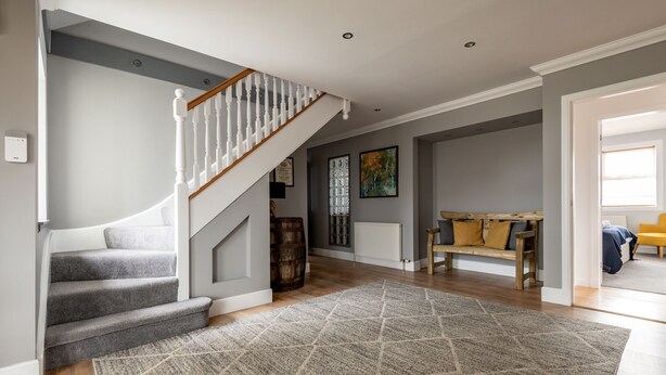 A staircase with a wooden handrail and carpeted steps, a wooden bench with cushions, a radiator, and a framed picture on the wall. - Rosemount | Kilrenny (Kilrenny)
