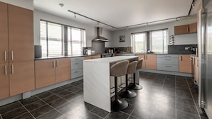 A modern kitchen with a central island, bar stools, and a large window. - Rosemount | Kilrenny (Kilrenny)