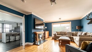 A modern living room with a sofa, ottoman, and a flat-screen TV. - Rosemount | Kilrenny (Kilrenny)