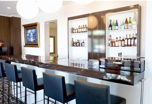 Een moderne bar met een lange toonbank, meerdere barkrukken en planken vol met verschillende flesjes drank.